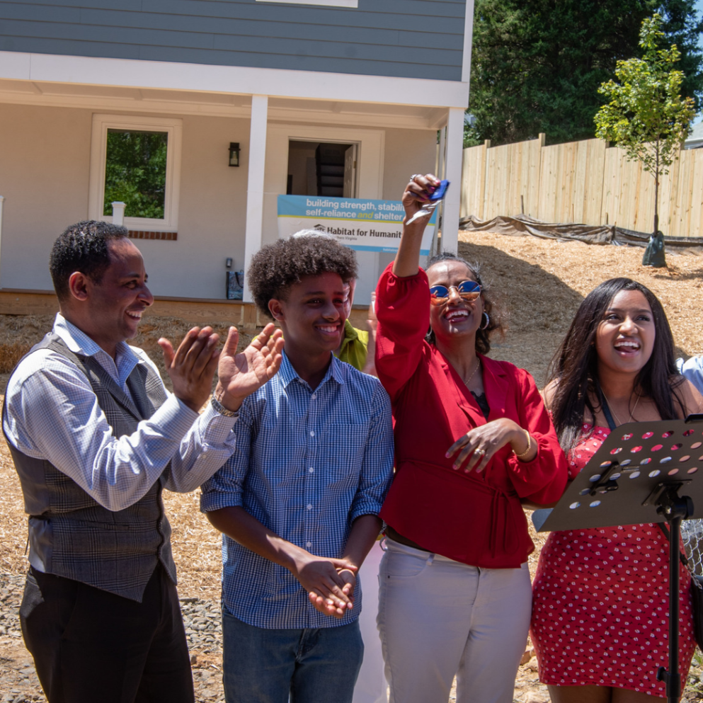 Family standing in front of their home. Woman has her home key in her raised hand.