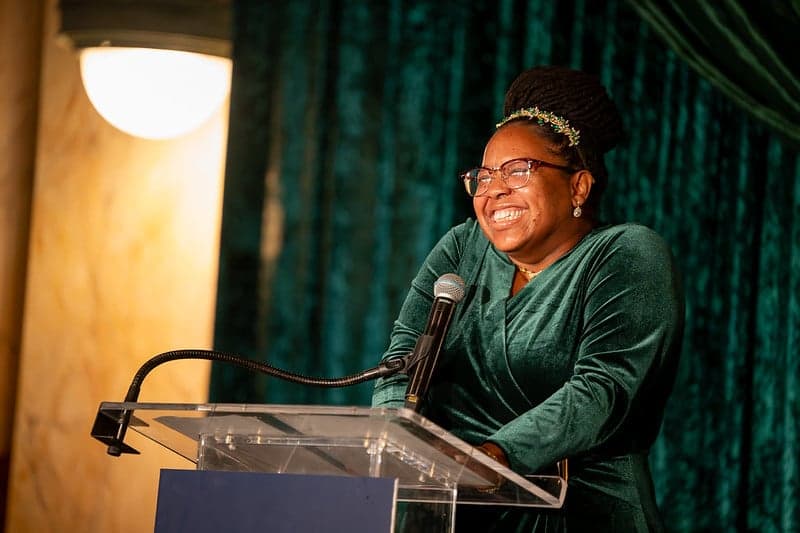 A woman standing at a podium with a large, beautiful smile.